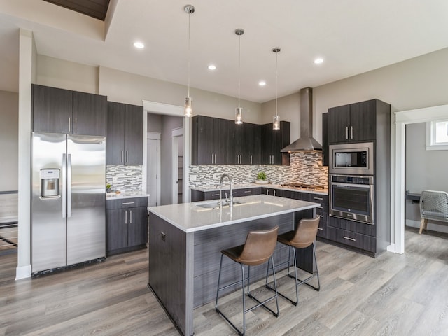 kitchen featuring appliances with stainless steel finishes, light hardwood / wood-style flooring, wall chimney exhaust hood, and backsplash