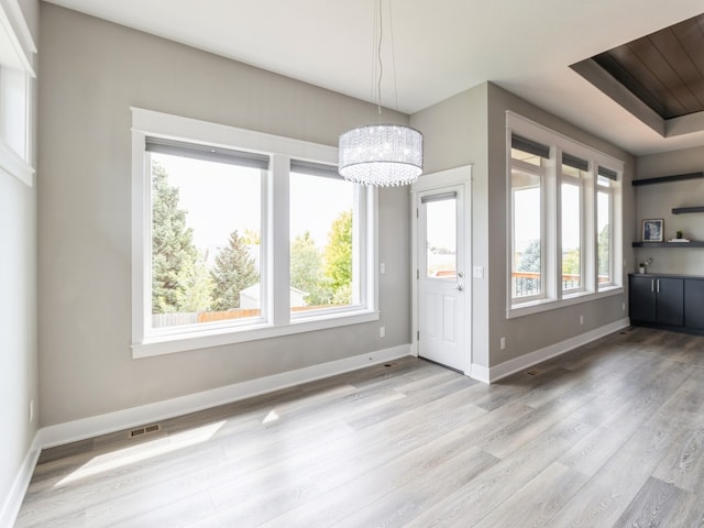 unfurnished dining area featuring a tray ceiling, a notable chandelier, and light hardwood / wood-style floors