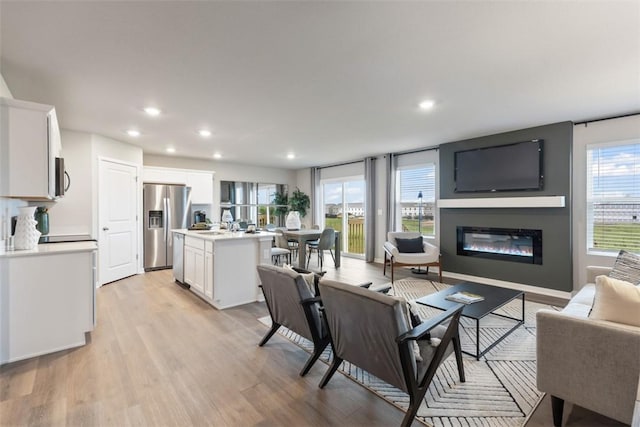 living room featuring recessed lighting, light wood-style flooring, and a glass covered fireplace