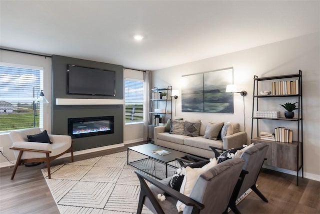 living area with a glass covered fireplace, recessed lighting, wood finished floors, and baseboards