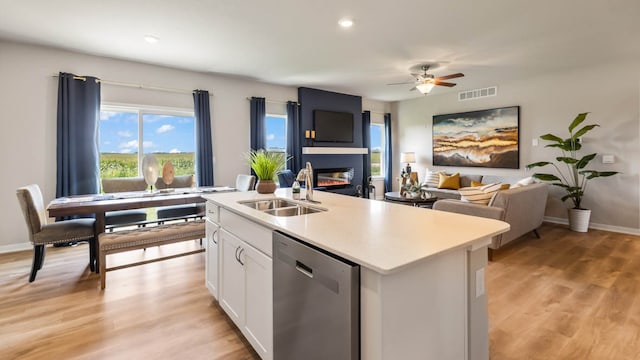 kitchen with dishwasher, a center island with sink, sink, a fireplace, and white cabinetry