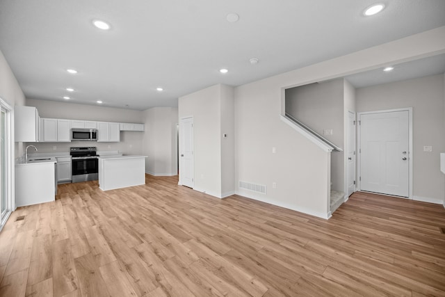 kitchen with sink, a kitchen island, white cabinetry, appliances with stainless steel finishes, and light wood-type flooring