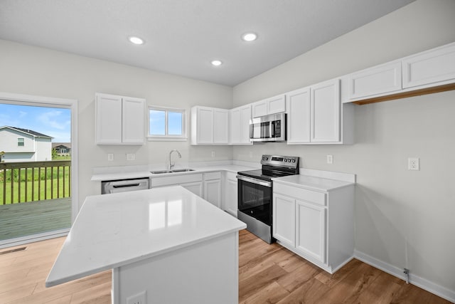 kitchen with a kitchen island, light wood-type flooring, stainless steel appliances, sink, and white cabinetry