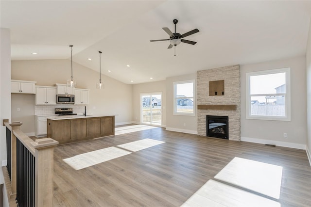 unfurnished living room with ceiling fan, sink, light hardwood / wood-style floors, lofted ceiling, and a fireplace