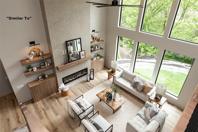 living area with wood finished floors, visible vents, a towering ceiling, a ceiling fan, and a glass covered fireplace