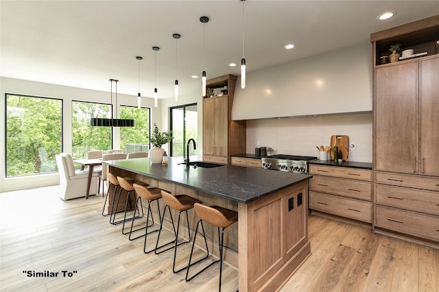 kitchen with a kitchen island with sink, a sink, a kitchen breakfast bar, light wood-type flooring, and decorative backsplash