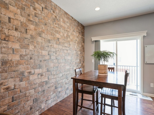 dining space featuring dark wood-type flooring, visible vents, brick wall, and a textured ceiling