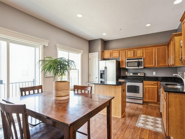 kitchen featuring a sink, dark countertops, hardwood / wood-style floors, a center island, and appliances with stainless steel finishes