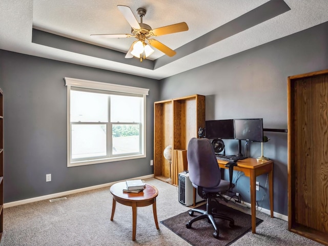 carpeted home office featuring a tray ceiling, visible vents, baseboards, and ceiling fan