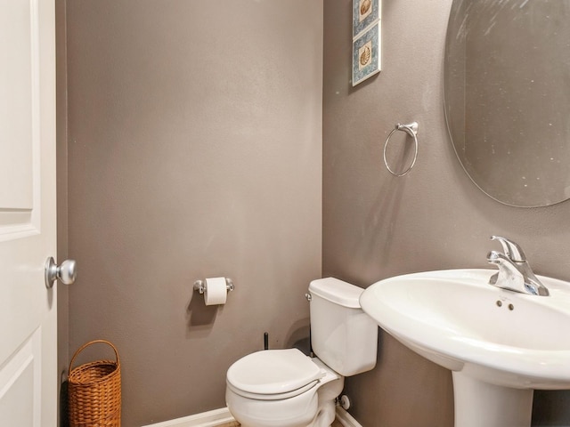 half bathroom featuring toilet, baseboards, and a sink