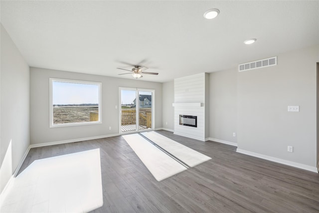 unfurnished living room featuring ceiling fan, a large fireplace, and dark hardwood / wood-style flooring