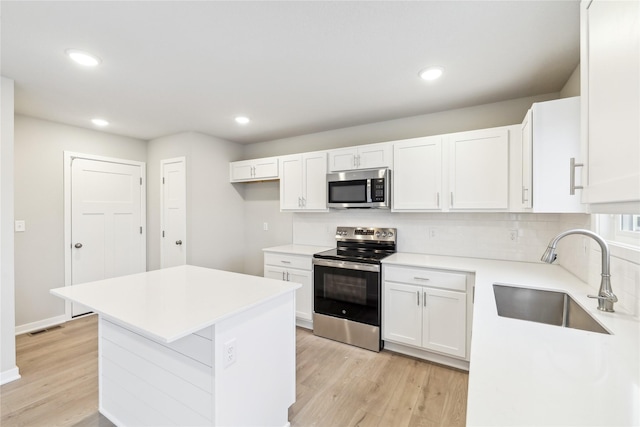 kitchen with stainless steel appliances, sink, light hardwood / wood-style flooring, white cabinetry, and tasteful backsplash