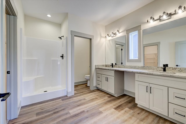 bathroom with double vanity, a stall shower, toilet, wood finished floors, and a sink