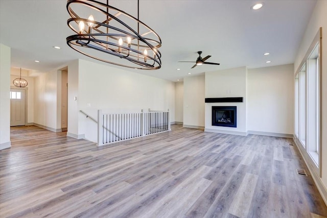 unfurnished living room featuring recessed lighting, baseboards, wood finished floors, a fireplace, and ceiling fan with notable chandelier