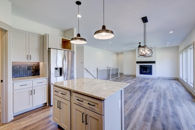 kitchen with light wood-type flooring, stainless steel refrigerator with ice dispenser, backsplash, a glass covered fireplace, and pendant lighting