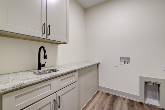 laundry area featuring washer hookup, wood finished floors, a sink, baseboards, and cabinet space