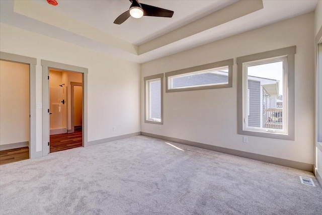 unfurnished bedroom featuring carpet floors, a ceiling fan, visible vents, baseboards, and a tray ceiling