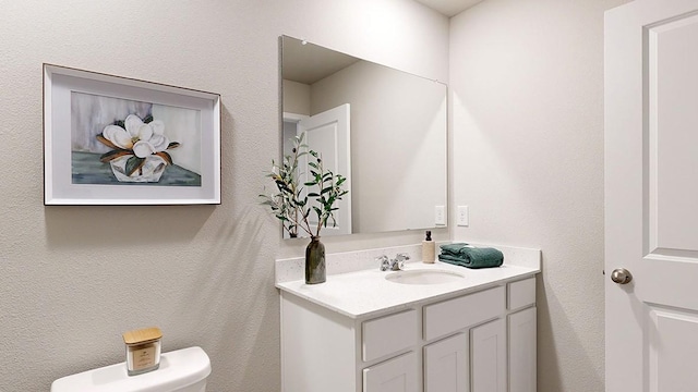 bathroom featuring toilet, vanity, and a textured wall