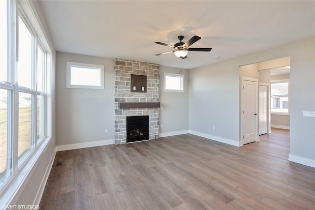 unfurnished living room featuring light wood-type flooring, a stone fireplace, and ceiling fan