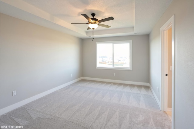 empty room featuring light colored carpet, a raised ceiling, and ceiling fan