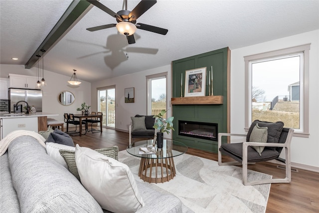 living area featuring vaulted ceiling with beams, a textured ceiling, a fireplace, wood finished floors, and baseboards