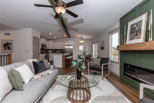 living room with lofted ceiling, a textured ceiling, wood finished floors, visible vents, and a glass covered fireplace