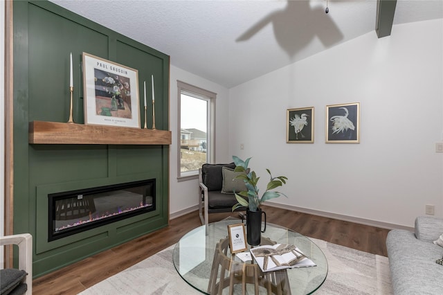 living room featuring a glass covered fireplace, lofted ceiling, baseboards, and wood finished floors