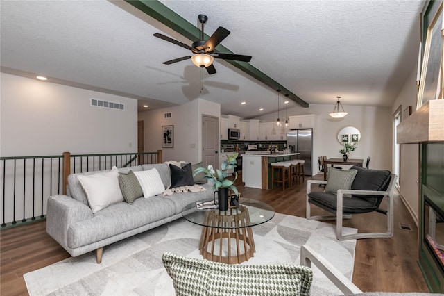 living area with lofted ceiling with beams, a textured ceiling, recessed lighting, wood finished floors, and visible vents