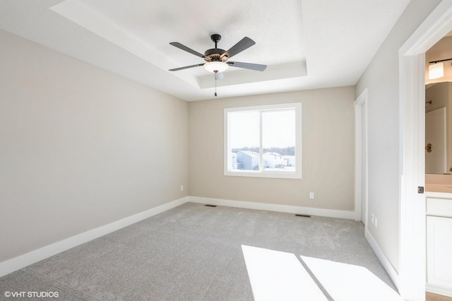 spare room featuring ceiling fan, light carpet, and a tray ceiling