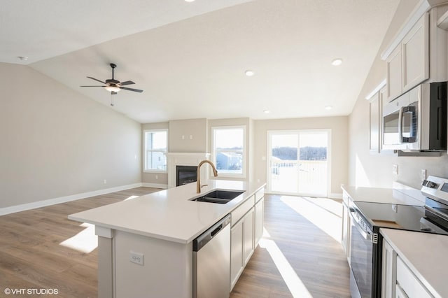 kitchen with sink, an island with sink, lofted ceiling, white cabinets, and appliances with stainless steel finishes