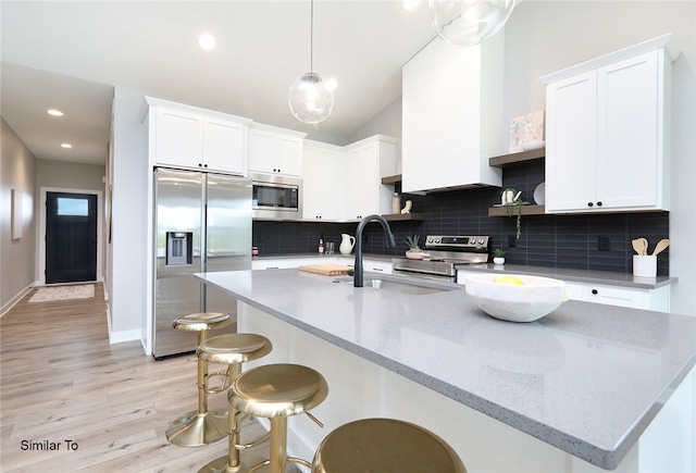 kitchen with pendant lighting, built in appliances, light hardwood / wood-style flooring, tasteful backsplash, and white cabinets