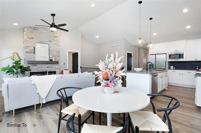 dining area with light hardwood / wood-style flooring, a stone fireplace, sink, high vaulted ceiling, and ceiling fan