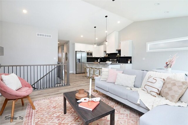 living room featuring light hardwood / wood-style flooring, vaulted ceiling, and sink