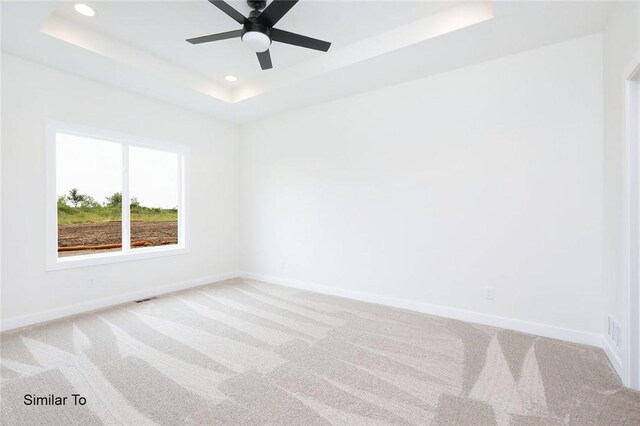 carpeted empty room with a raised ceiling and ceiling fan