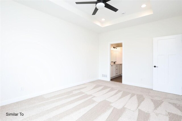 unfurnished bedroom with light colored carpet, connected bathroom, ceiling fan, and a tray ceiling