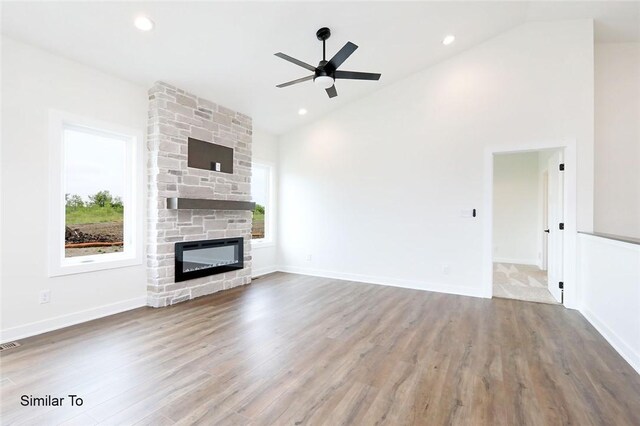 unfurnished living room featuring wood-type flooring, a healthy amount of sunlight, and a stone fireplace