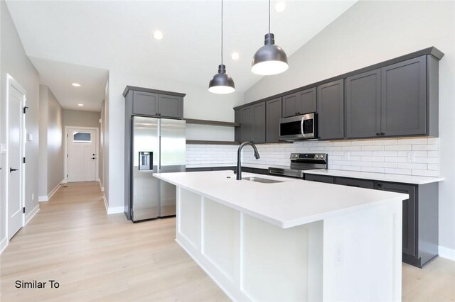 kitchen with light hardwood / wood-style flooring, stainless steel appliances, sink, decorative backsplash, and a center island with sink