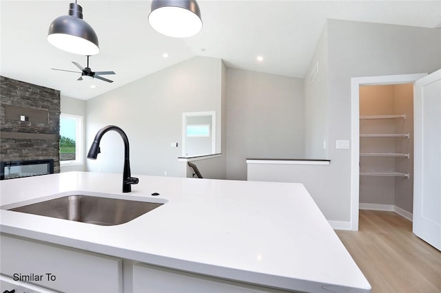 kitchen with light wood finished floors, pendant lighting, light countertops, vaulted ceiling, and a sink