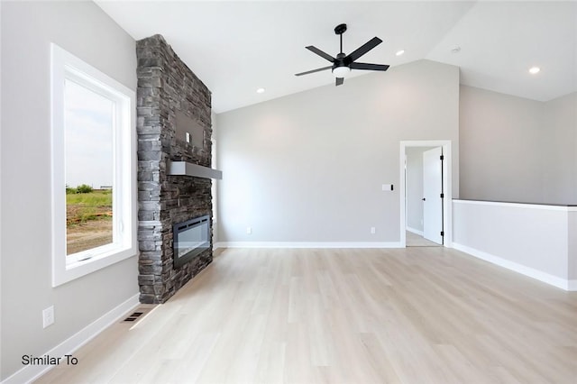 unfurnished living room with baseboards, lofted ceiling, a stone fireplace, and wood finished floors