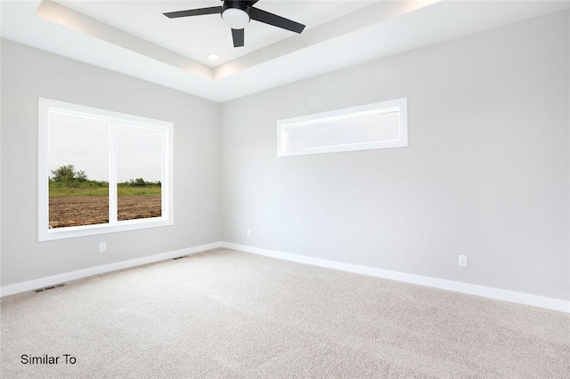 empty room with a tray ceiling, carpet, visible vents, and baseboards