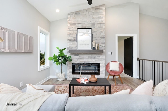 living area featuring baseboards, lofted ceiling, a stone fireplace, and wood finished floors