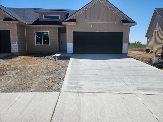 view of front of house featuring board and batten siding, driveway, a garage, central AC unit, and roof with shingles