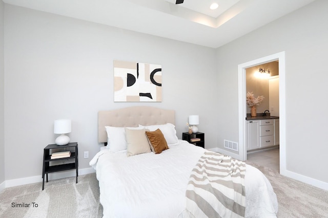 bedroom with visible vents, baseboards, light colored carpet, and connected bathroom