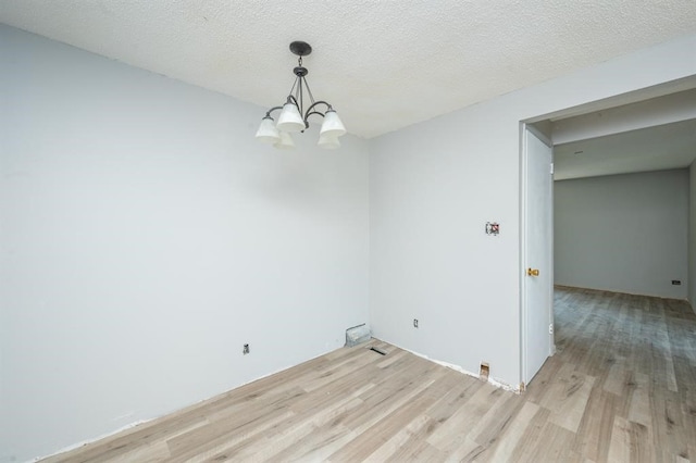 spare room with a textured ceiling, light hardwood / wood-style flooring, and a notable chandelier