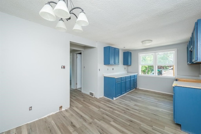 1125 Clinton Ave, Des Moines, IA 50313 - kitchen featuring blue cabinets, light wood-type flooring, light countertops, a textured ceiling, and baseboards