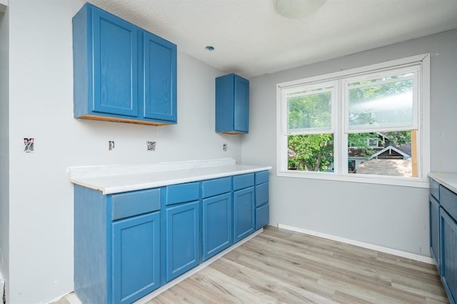 1125 Clinton Ave, Des Moines, IA 50313 - kitchen with blue cabinets, light wood-style flooring, light countertops, and baseboards