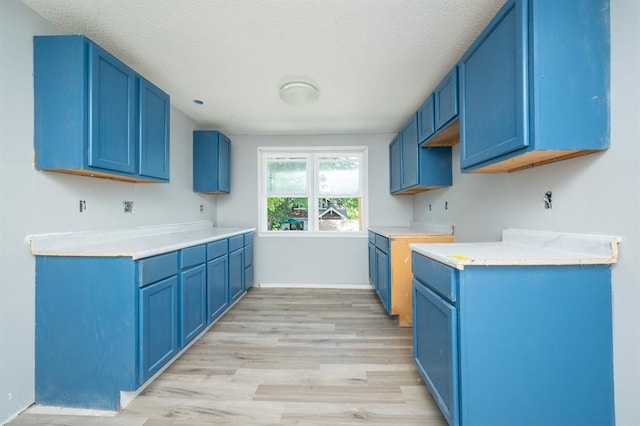 1125 Clinton Ave, Des Moines, IA 50313 - kitchen with blue cabinets, light wood-type flooring, light countertops, a textured ceiling, and baseboards