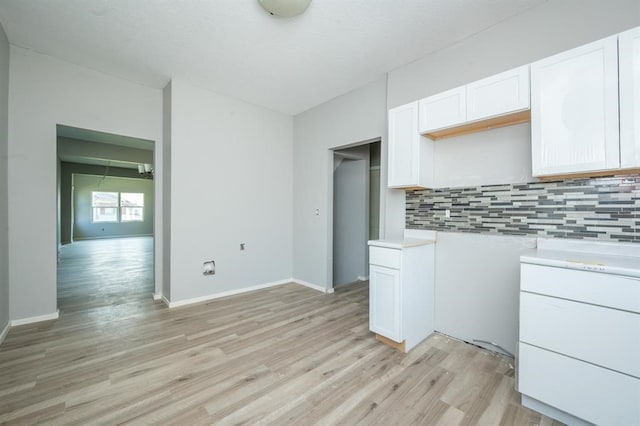 1125 Clinton Ave, Des Moines, IA 50313 - kitchen with light wood-style floors, backsplash, light countertops, white cabinetry, and baseboards