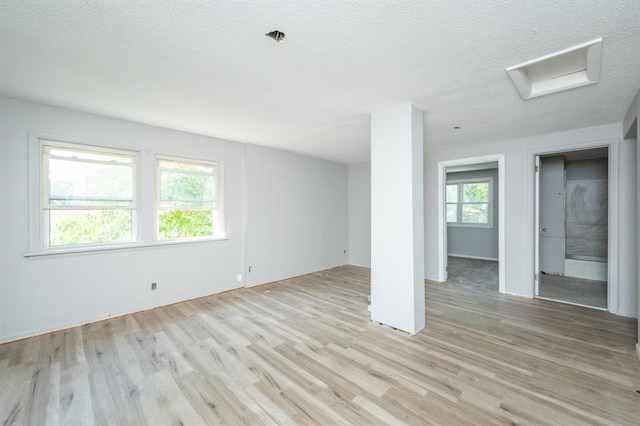 unfurnished room with light wood-type flooring, a healthy amount of sunlight, and a textured ceiling