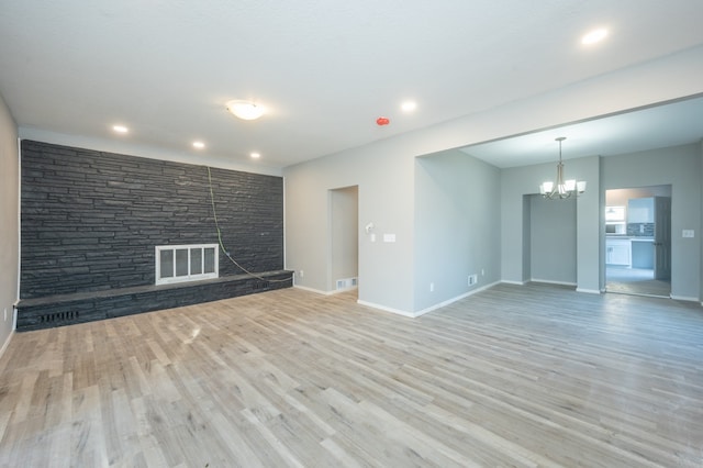 unfurnished living room featuring a stone fireplace, a notable chandelier, and light wood-type flooring